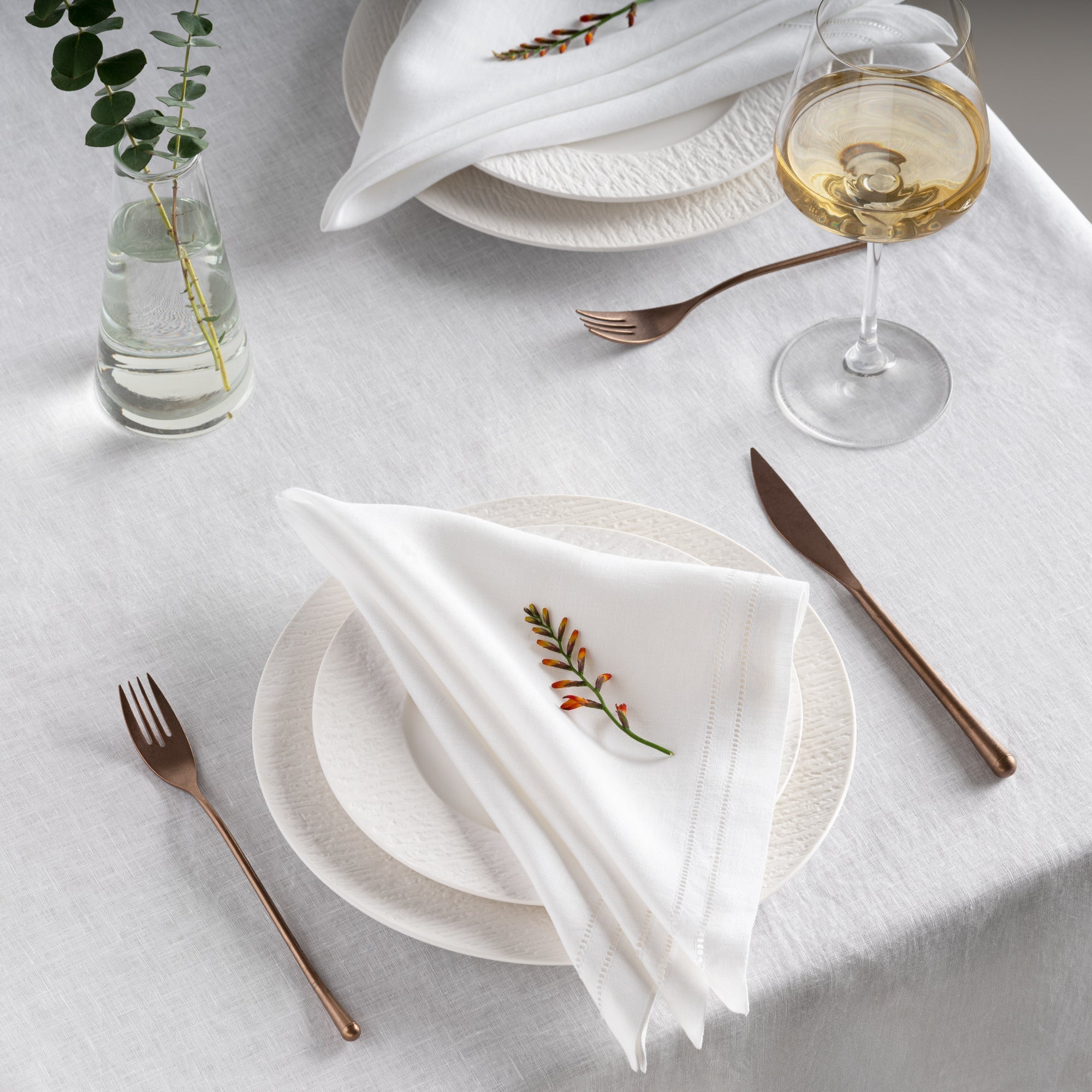 white linen napkins with elegant double hemstitched lines setting on beautiful white linen table cloth, ceramic plates and gold cutlery sets