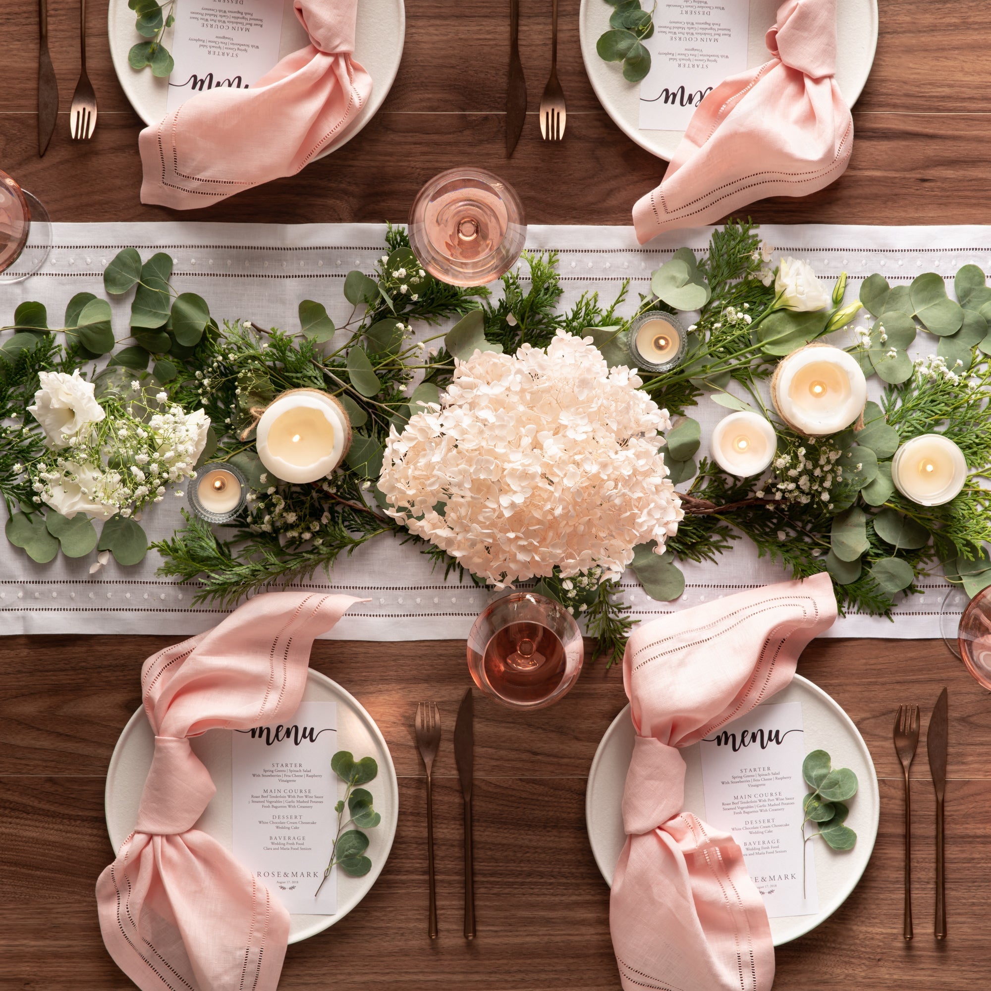 blush pink linen napkins with elegant double hemstitching lines setting on beautiful wedding tablescape for four on farmhouse table with ceramic plates and gold cutlery set, twilight candles, dried flowers and wine glass